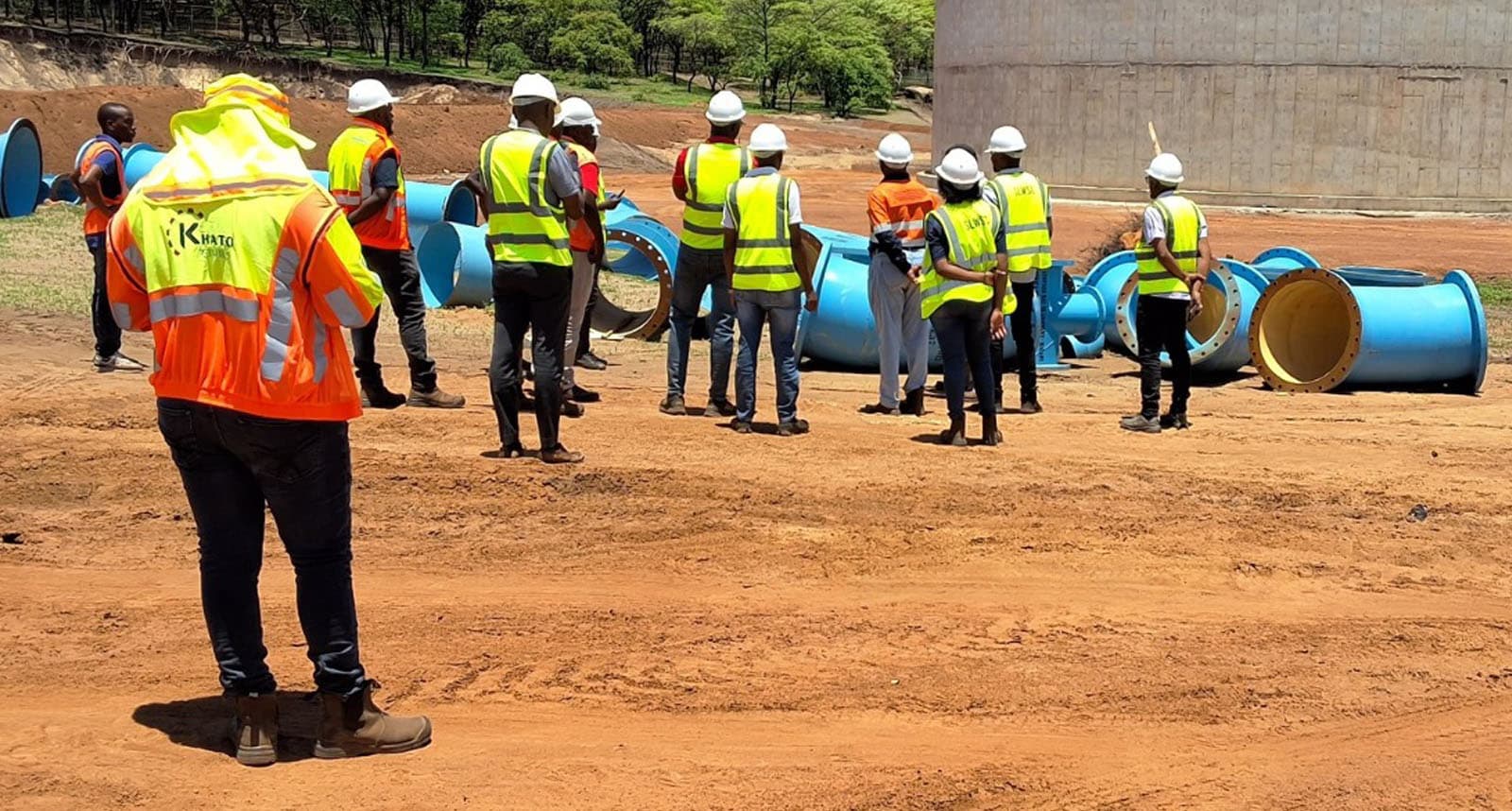 Engineers in high-visibility gear at a construction site with industrial pipes